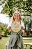 Eine Gastgeberin mit ihrer Plakette der Auszeichnung Goldener Gockel - Gastfreundlichster Ferienhof Bayerns im Dirndl im Garten ihres Urlaubsbauernhofes.