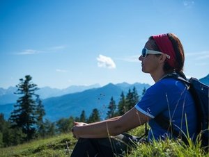 Wanderin sitzt und erholt sich in Bergwiese vor Bergpanorama