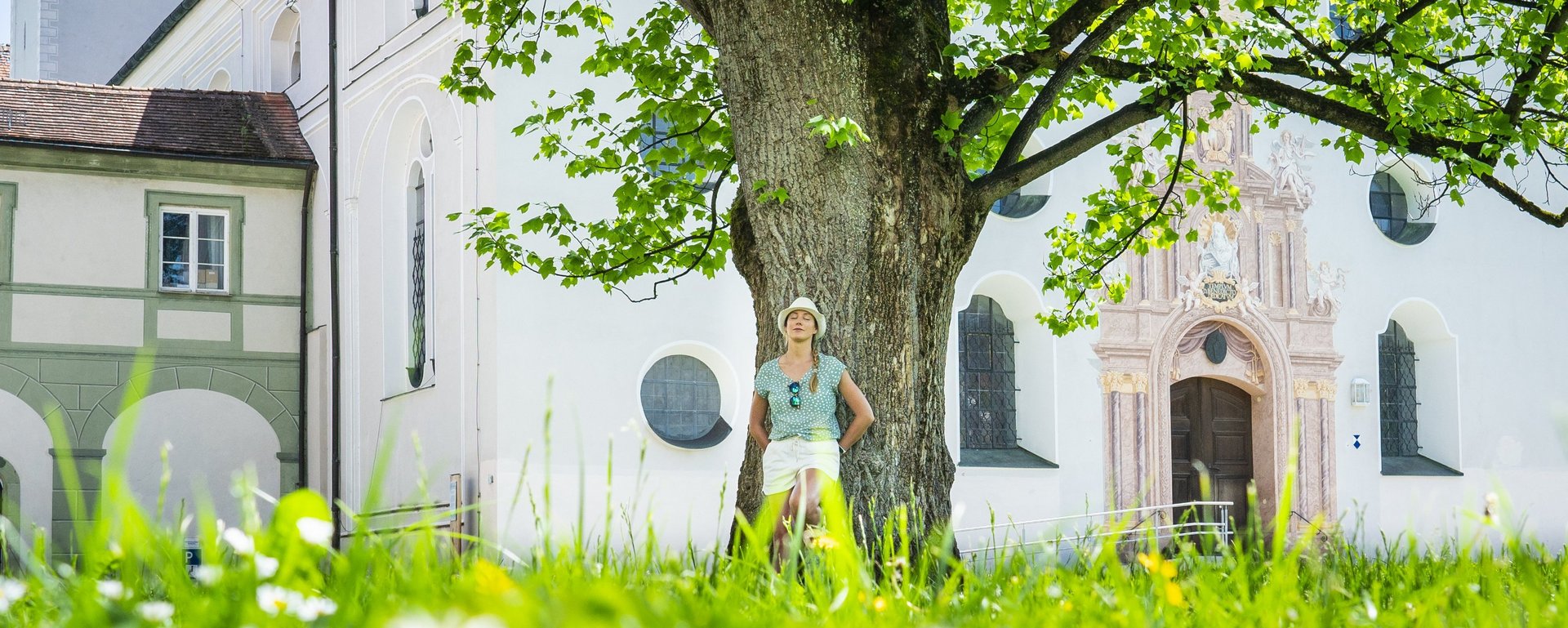 Frau lehnt entspannt am Baum vor dem Kloster Benediktbeuern